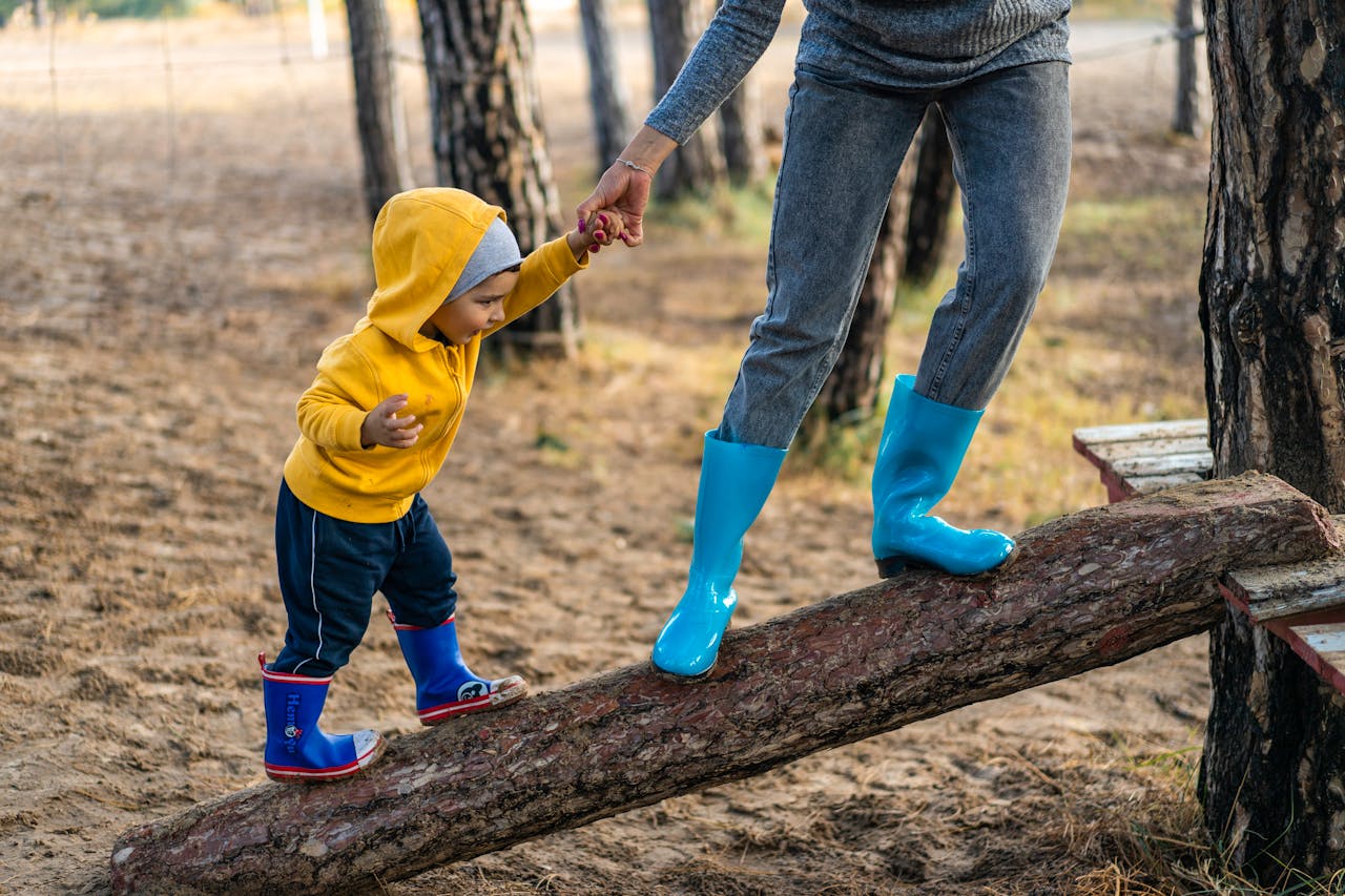 Assistante maternelle 86800 Jardres St julien l'ars, Pouillé, Tercé, Bonnes, Lavoux, Chauvigny A woman helps her toddler walk on a log in a park, showcasing child support and family bonding.