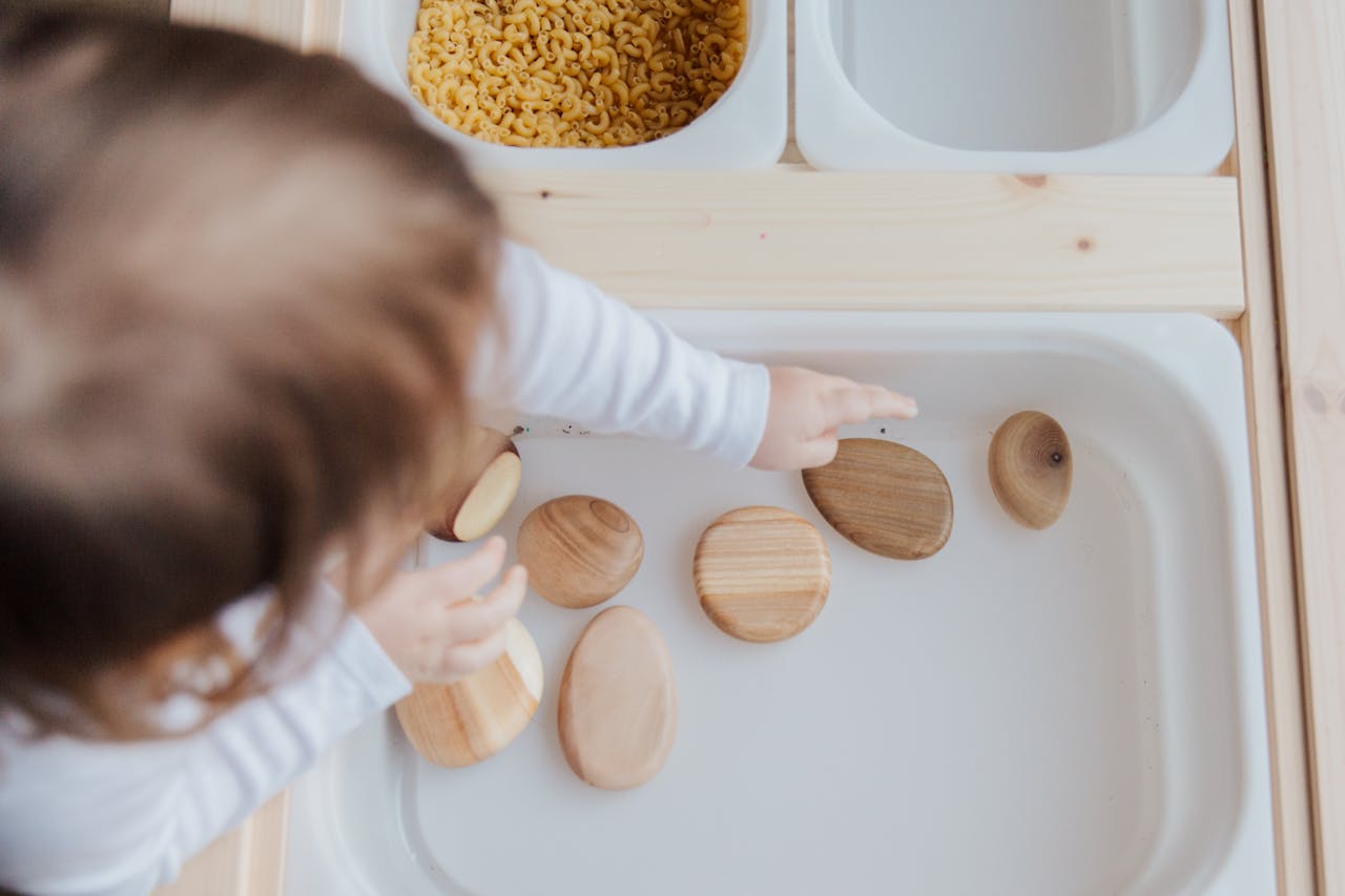 A toddler playing with wooden stones in a Montessori educational setup, promoting motor skills development.
