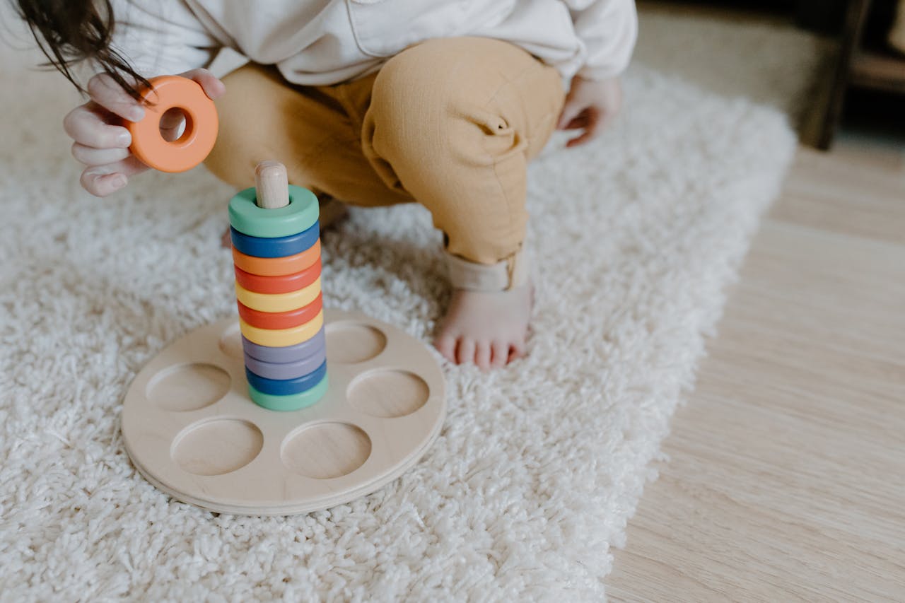 Assistante maternelle 86800 Jardres St julien l'ars, Pouillé, Tercé, Bonnes, Lavoux, Chauvigny A child playing with a wooden ring stacking toy on a carpet indoors.